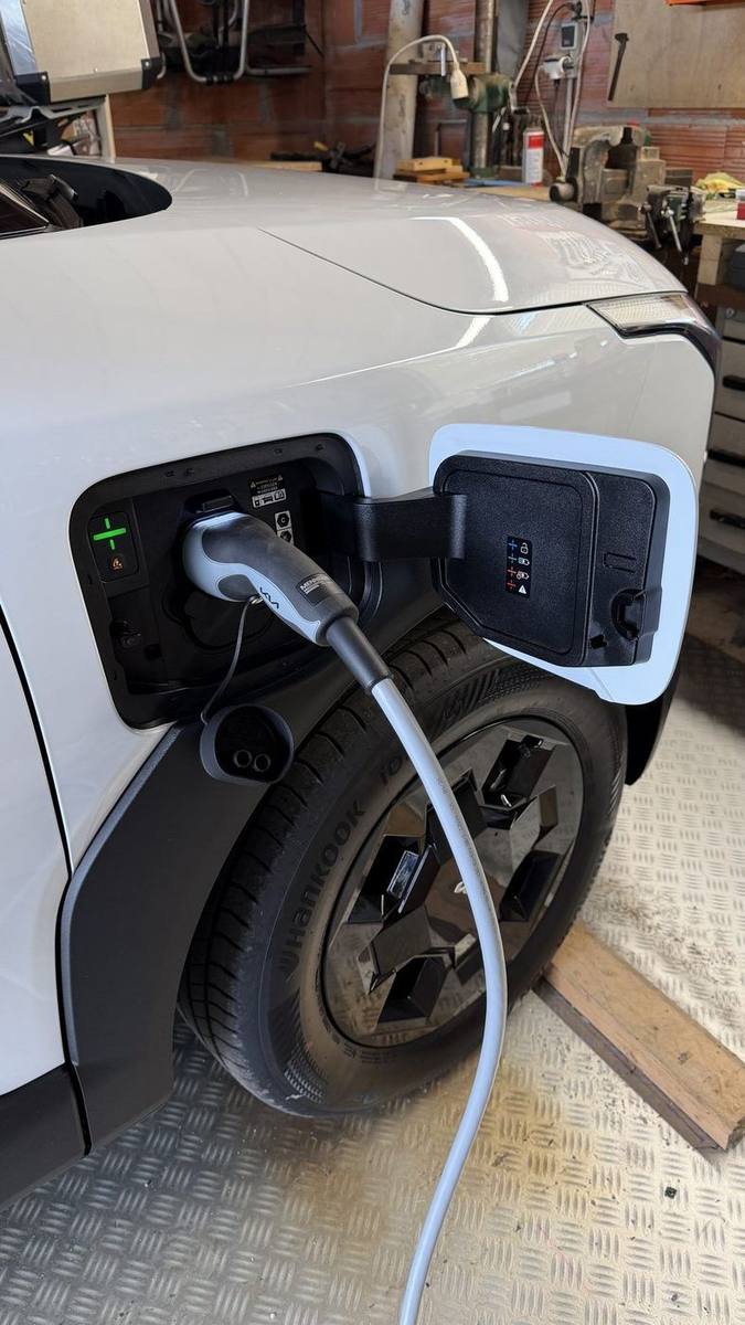 Véhicule électrique blanc garé dans un garage, câble de recharge branché sur la trappe de charge ouverte à l'avant